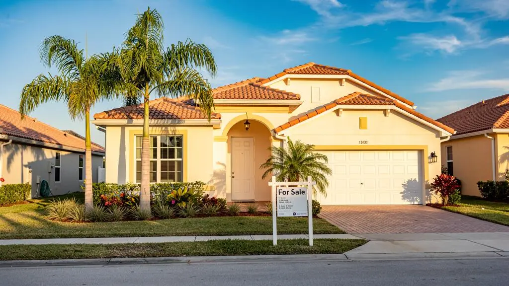 Maison résidentielle typique de Floride avec architecture subtropicale, stucco et toiture en tuiles, panneau à vendre dans le jardin